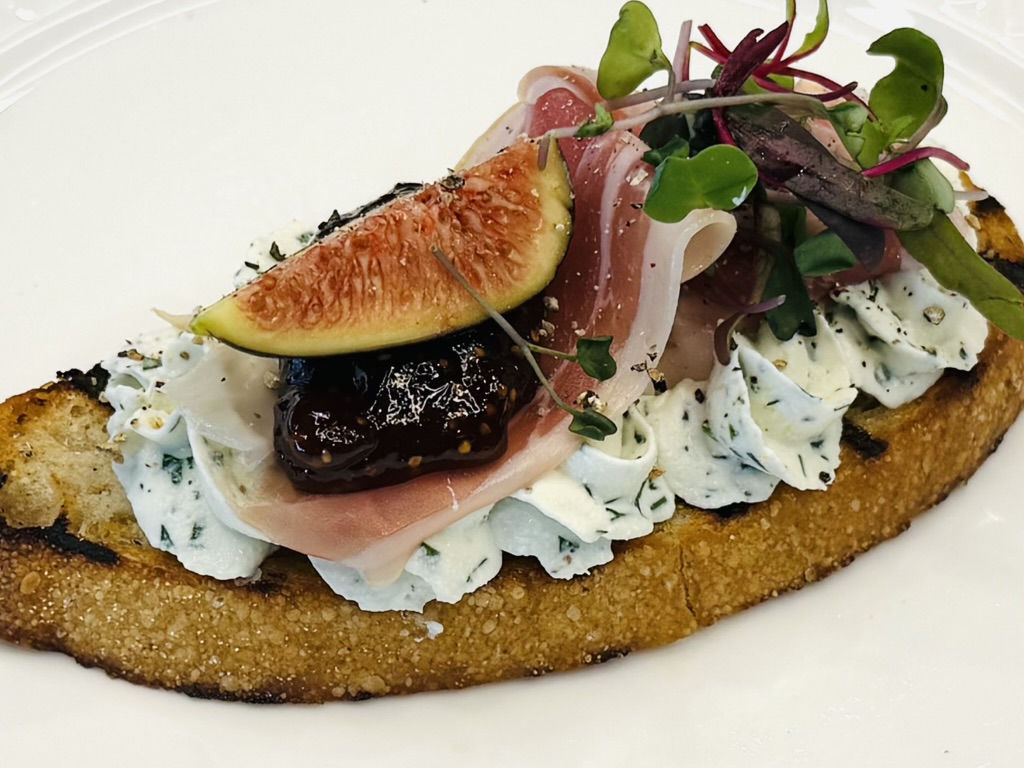 Single crostini with fig, prosciutto, herbed cheese and microgreens